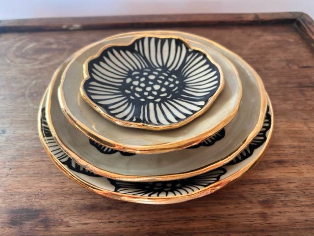 Stacked set of handmade flower-shaped ceramic dishes in various sizes with black floral patterns and 22K gold accents.