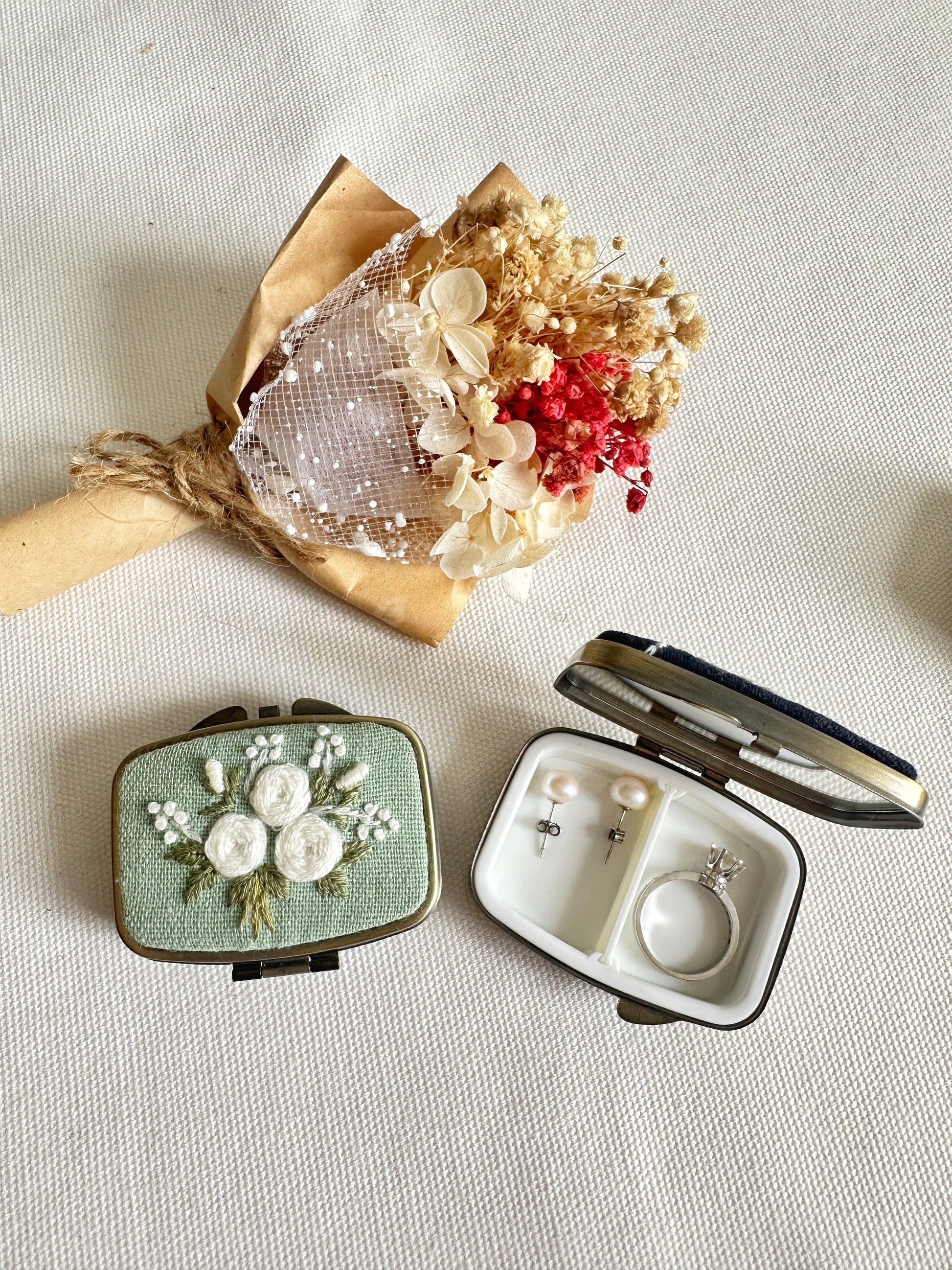 Green Floral Embroidered Jewelry Box - Elegant Storage featuring white rose embroidery, open to reveal ring and earring compartments beside dried flowers.