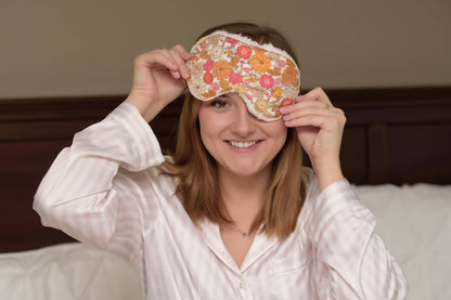 Woman smiling in pajamas while holding Sweet Dreams Cotton Sleep Mask with orange floral print, perfect for bedtime relaxation.