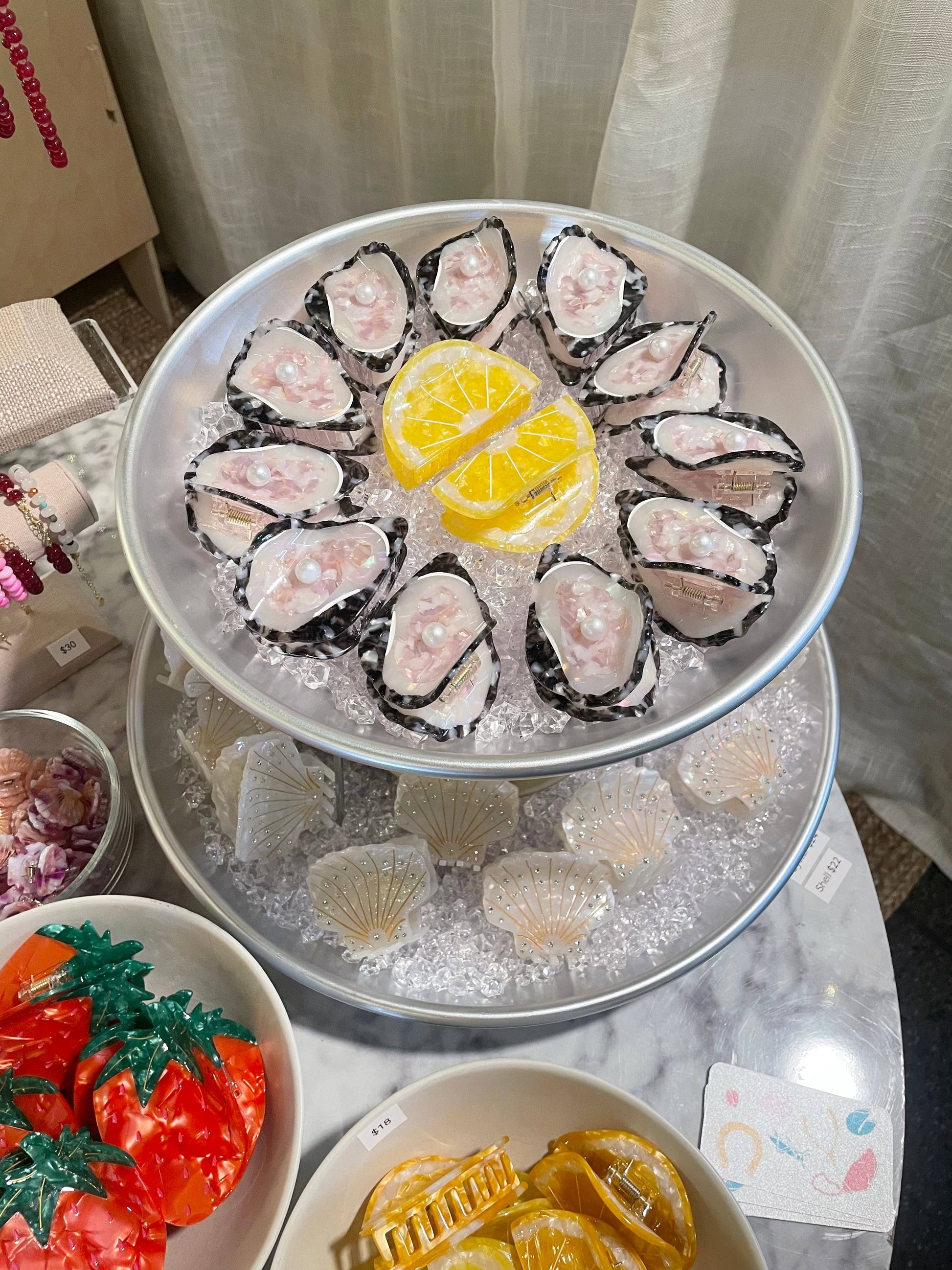 Display of Line&Co Oyster Claw Clips with Pearl on ice tray at boutique. Eye-catching hair accessories styled like oysters with lemon decor.