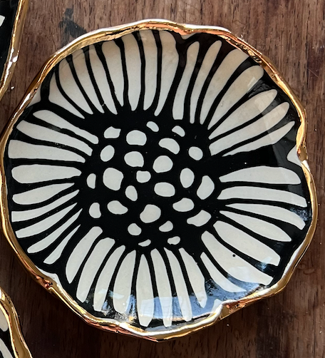 Detailed view of a 4" handmade ceramic dish featuring a daisy-inspired black floral motif and 22K gold edging.