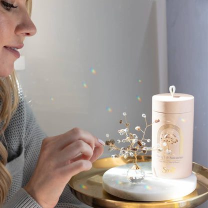 Close-up of woman adjusting Rose Quartz Suncatcher Tree of Life on a tray, with rainbow light reflections and elegant packaging nearby.