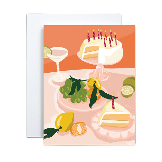Copper & Print's Birthday Greeting Card Handmade for Celebrations features an illustration of a birthday cake with candles, cake slices, a cocktail glass, green grapes, limes, a tangerine, and a lemon on a peach-toned table.
