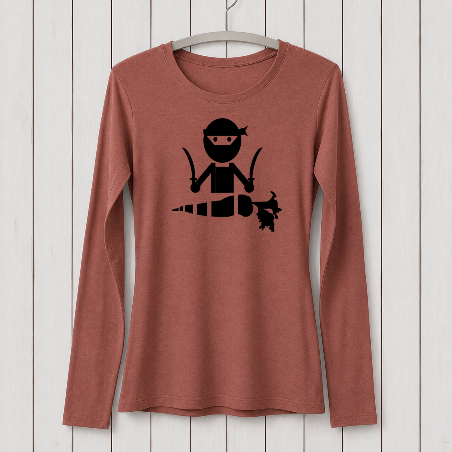Rust-colored long sleeve T-shirt with a black graphic of a ninja character holding a carrot, made from bamboo organic cotton, displayed on a white hanger against a wooden background.