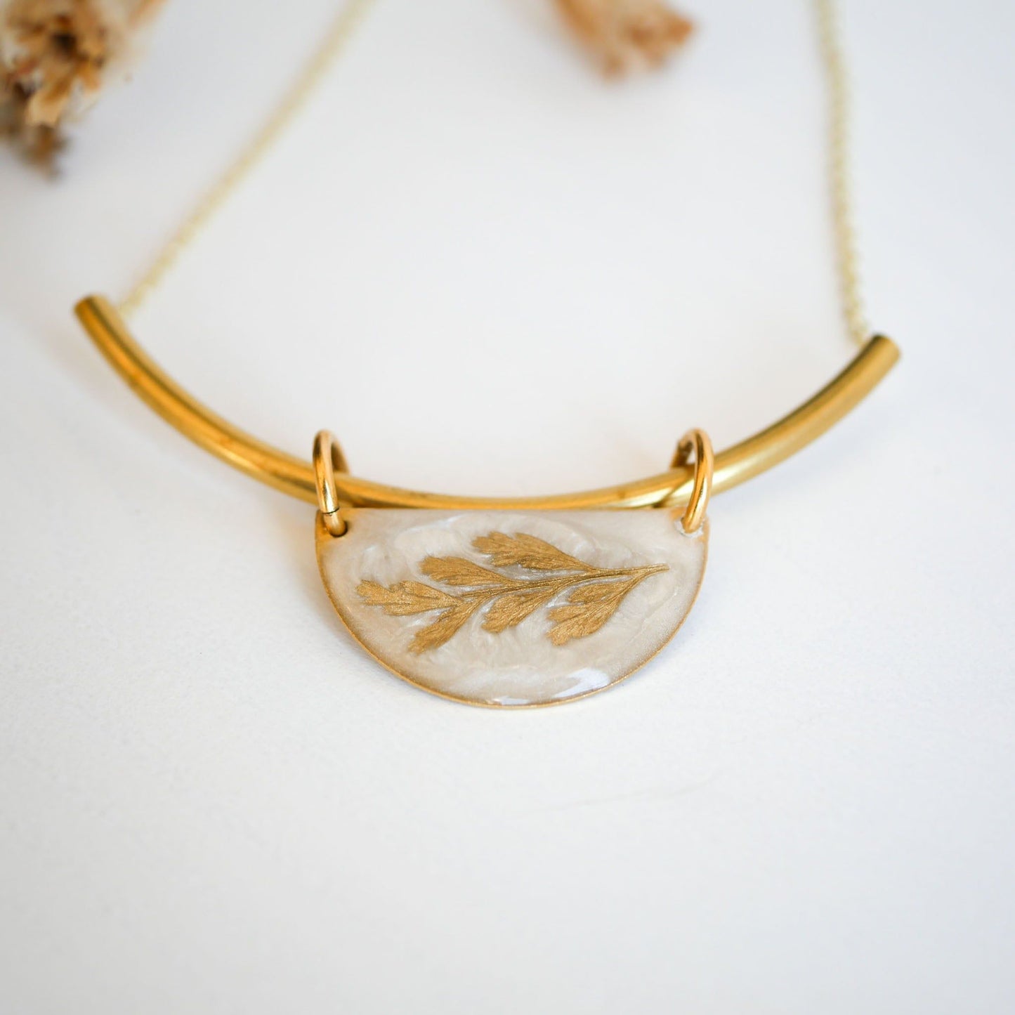 Close-up of Shield-style Midas Collection Necklace with a golden fern in resin, suspended from a curved gold bar for a modern classic look.