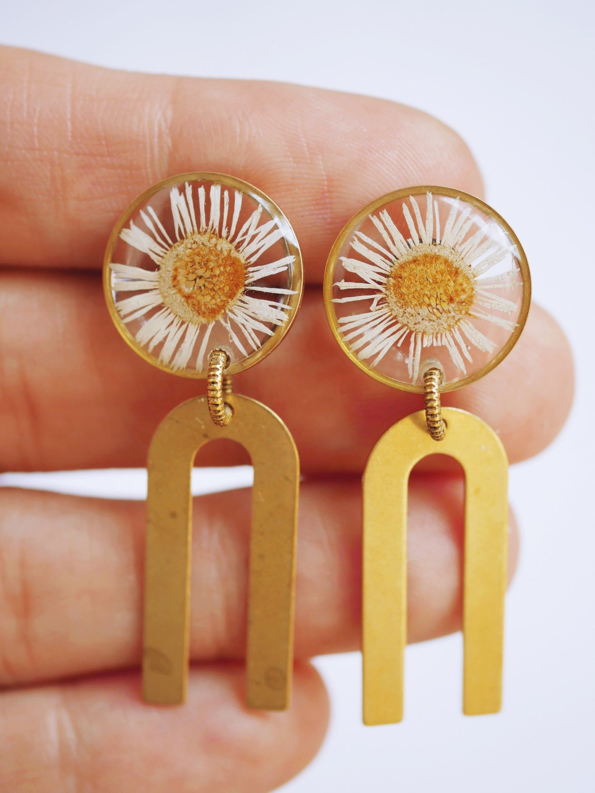 Hand holding Daisy Chime Earrings - Hope Symbol Jewelry with wild daisy flowers and gold chime arches. Artisan-crafted floral earrings by Seed&SoilShop.