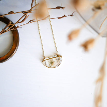 Meadow Luna Necklace with gold-plated chain and botanical resin pendant displayed on white surface with dried floral accents.