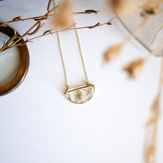 Meadow Luna Necklace with gold-plated chain and botanical resin pendant displayed on white surface with dried floral accents.