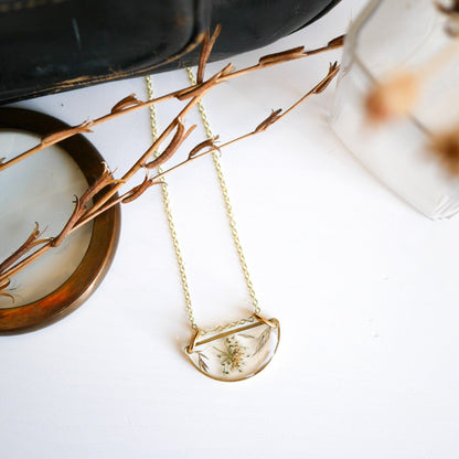 Flat lay of Meadow Luna Necklace with gold chain and botanical resin pendant styled with dried plants and vintage decor.
