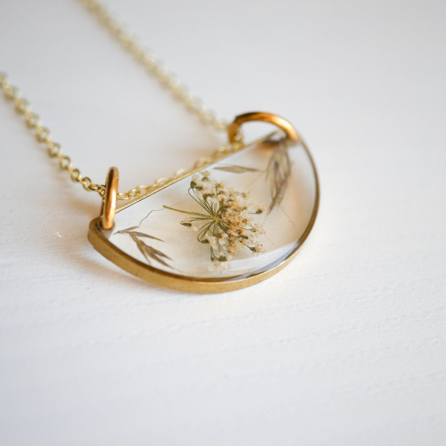Close-up of Meadow Luna Necklace featuring pressed botanical design in a clear resin half-moon pendant with vintage gold frame.