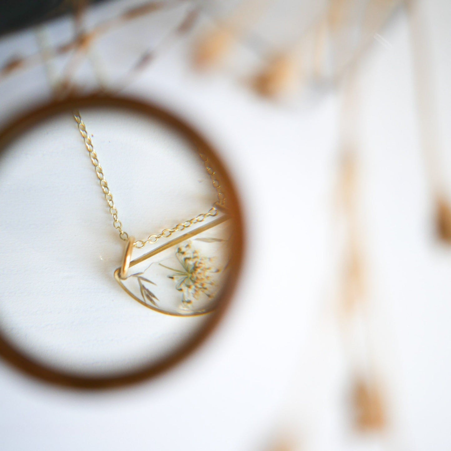 Artistic view of Meadow Luna Necklace through magnifying glass, emphasizing intricate botanical details in resin pendant.