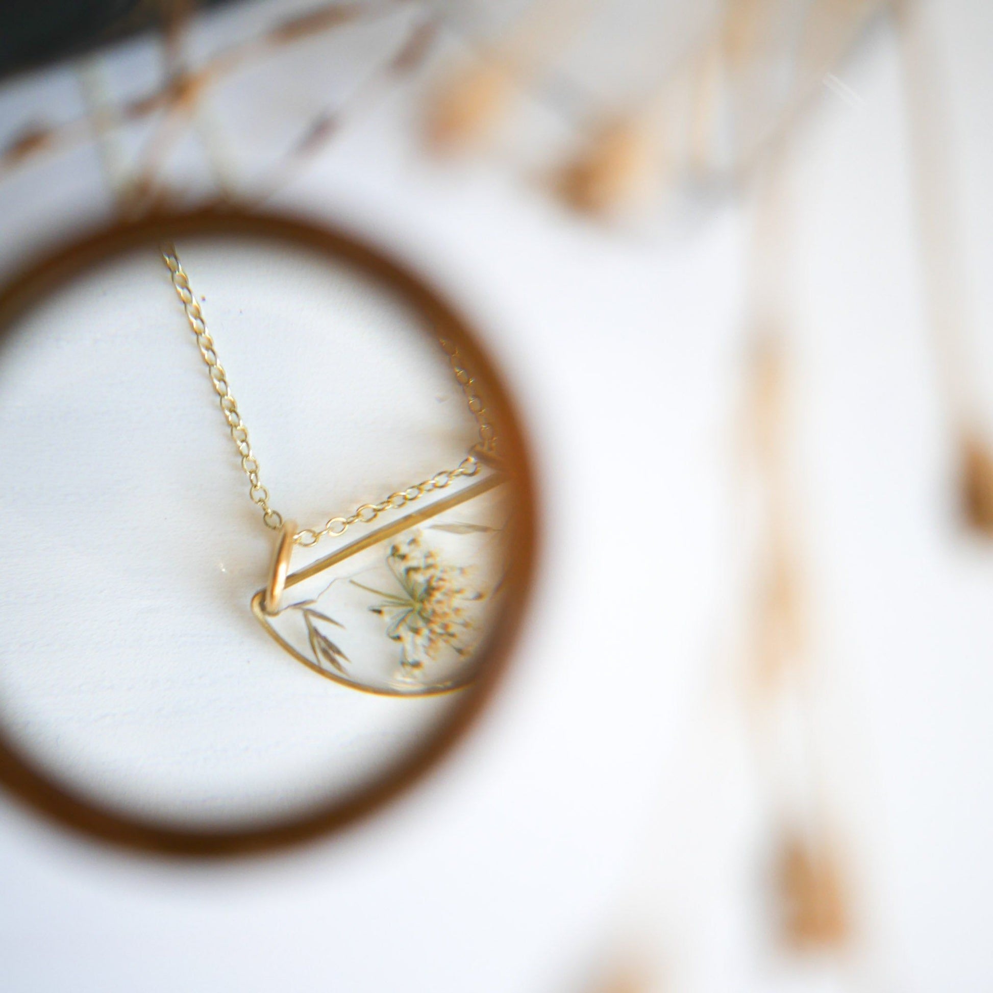 Artistic view of Meadow Luna Necklace through magnifying glass, emphasizing intricate botanical details in resin pendant.