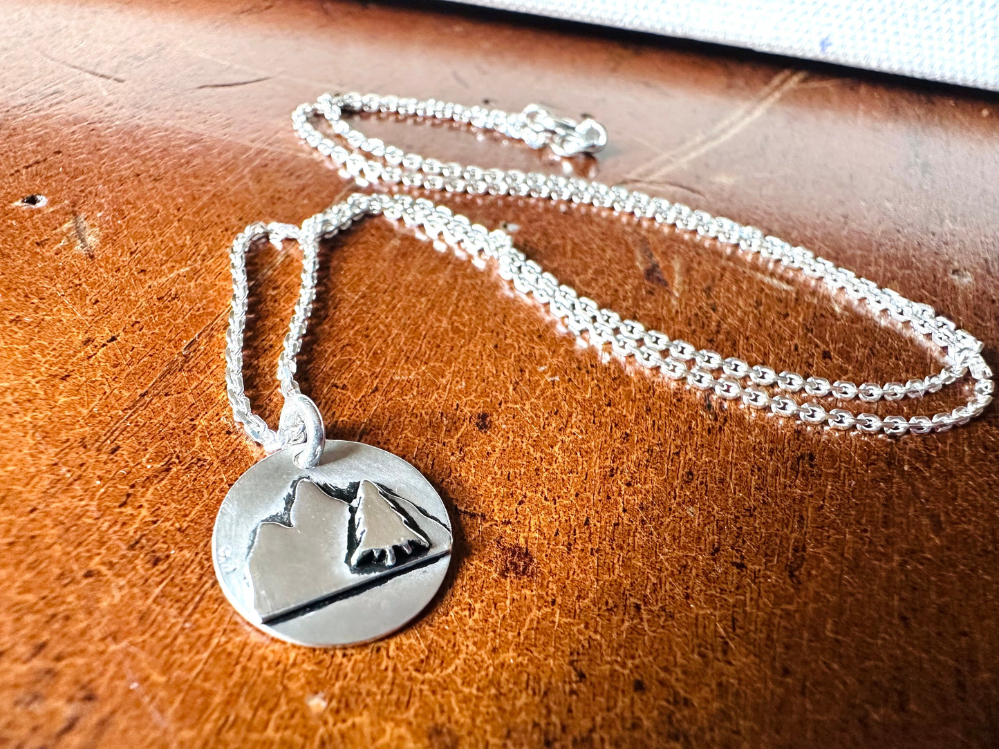 Silver mountain pendant necklace on wooden surface