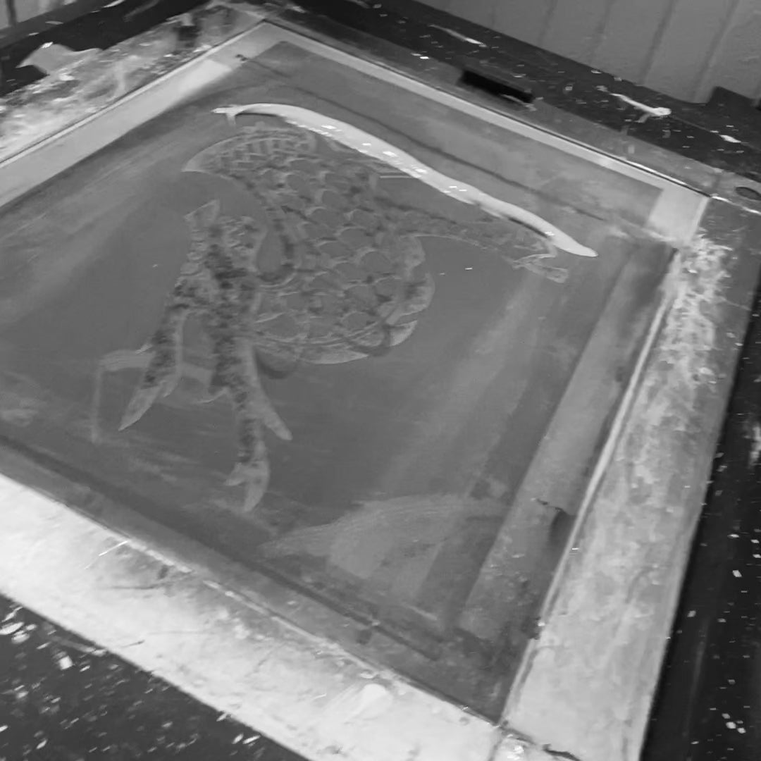 Black and white screen printing frame with dragon design used for 'Dare More' T-shirt. Behind-the-scenes of Uni-T's eco-friendly tee production.