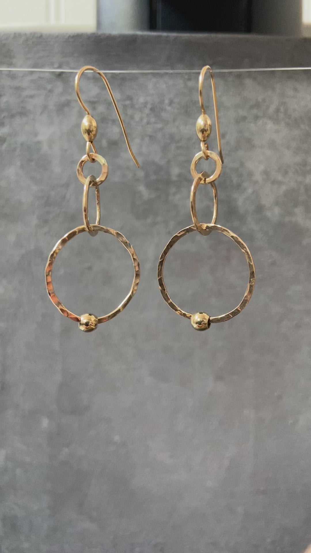 Gold HoopLink Earrings with textured hoops and bead accents, suspended against a dark gray backdrop to highlight craftsmanship.