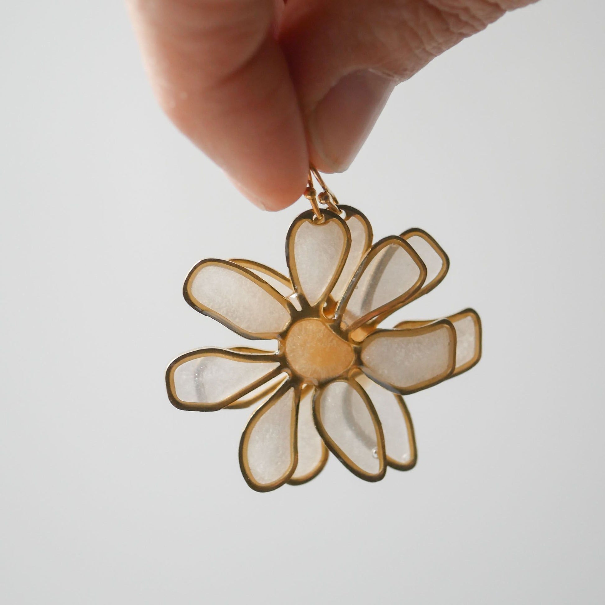 Hand holding peach daisy stained glass earring against light background. Unique summer accessory, handcrafted floral design.