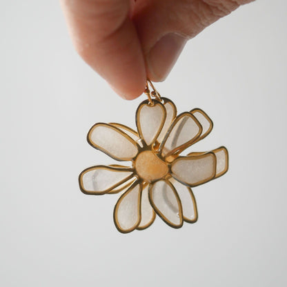 Hand holding peach daisy stained glass earring against light background. Unique summer accessory, handcrafted floral design.
