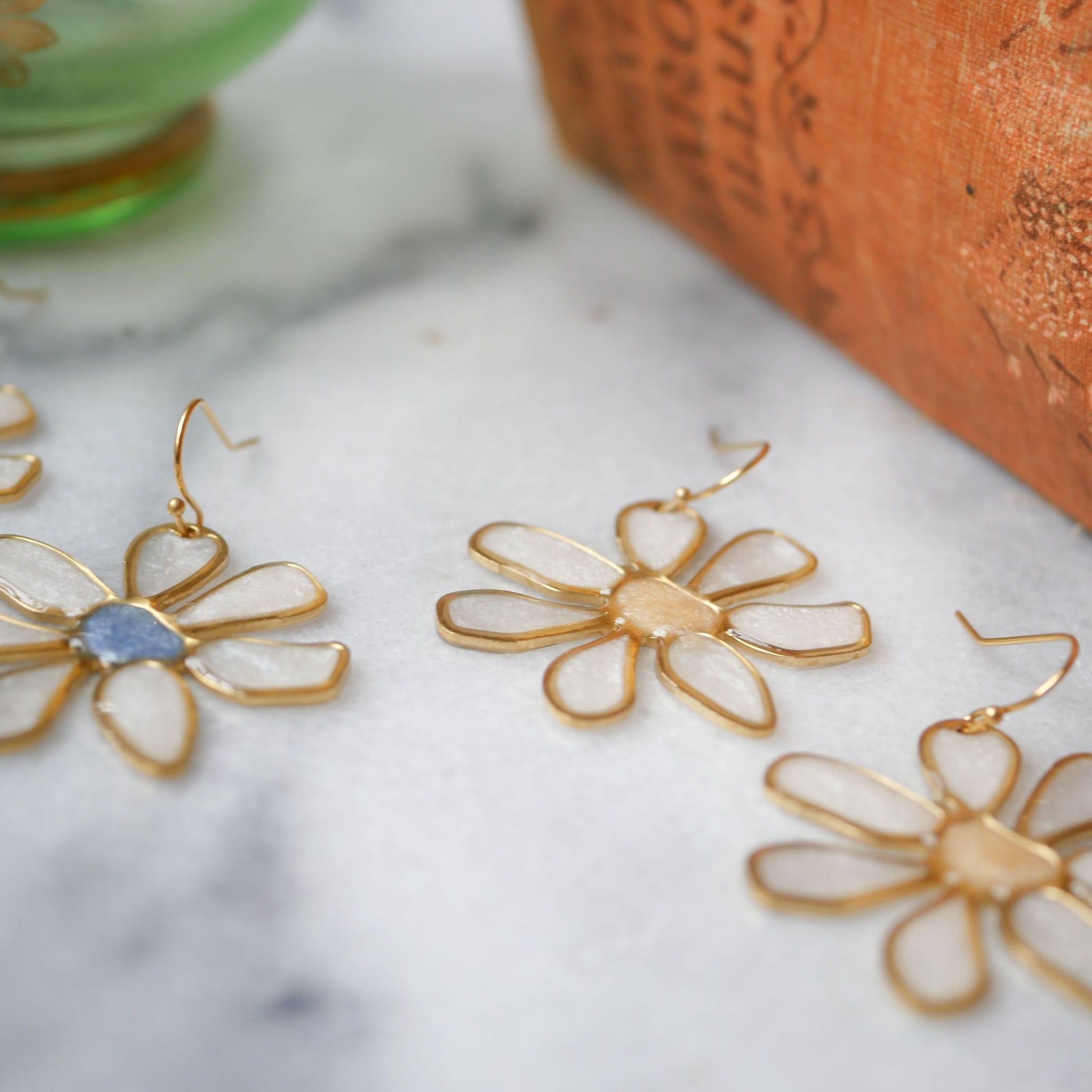 Assorted daisy stained glass earrings with gold trim on marble surface. Summer jewelry collection from Seed&SoilShop, shop now.