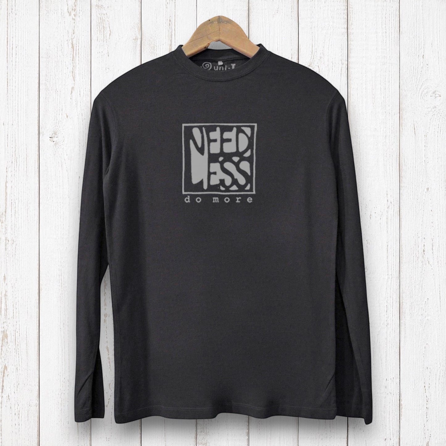 Uni-T black long sleeve bamboo graphic tee with Need Less Do More typography on a white wood background