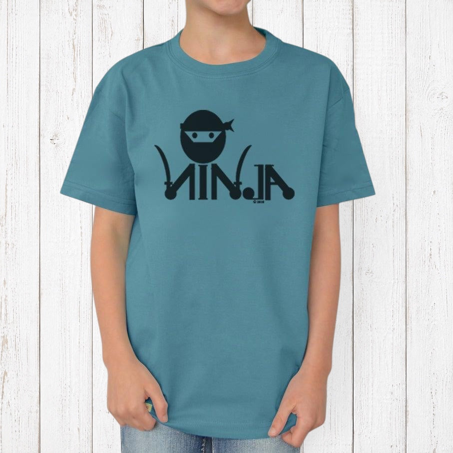 Uni-T kids blue organic cotton t-shirt featuring a black ninja graphic, worn by a child against a white wood wall.