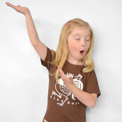 Young girl singing while wearing a brown Uni-T organic cotton t-shirt featuring a hand-illustrated rooster graphic
