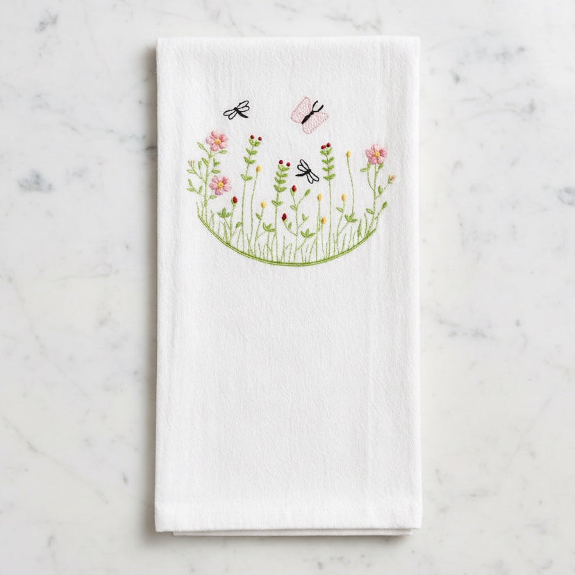 Uni-T white flour sack kitchen towel featuring delicate embroidery of pink flowers, green stems, and flying insects.