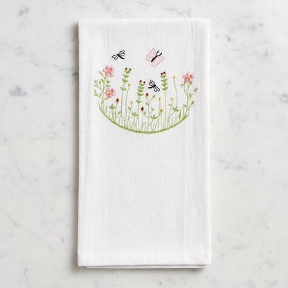 Uni-T white flour sack kitchen towel featuring delicate embroidery of pink flowers, green stems, and flying insects.