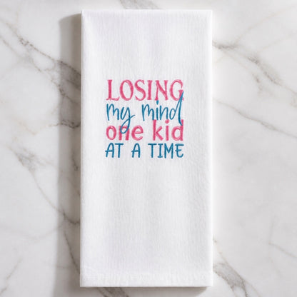 Uni-T white flour sack kitchen towel with pink and blue embroidered text reading Losing my mind one kid at a time