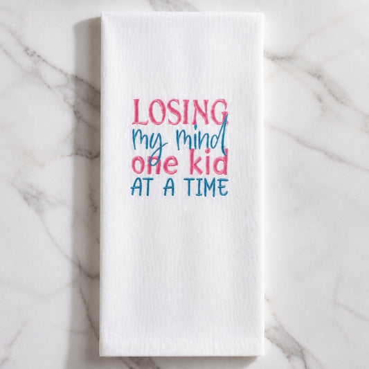 Uni-T white flour sack kitchen towel with pink and blue embroidered text reading Losing my mind one kid at a time