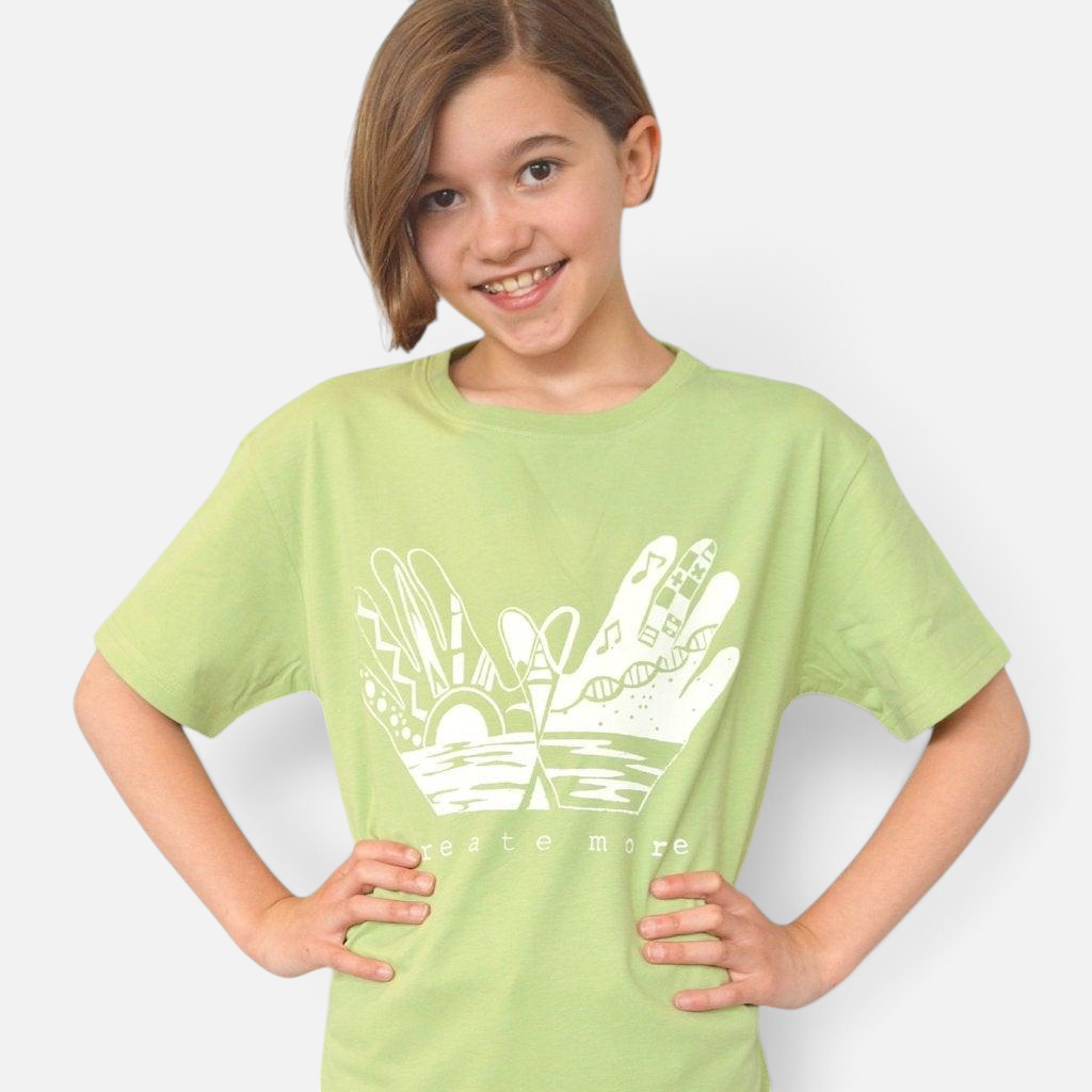 A young girl wearing a light green Uni-T organic cotton t-shirt with a white Create More hand-drawn graphic print.