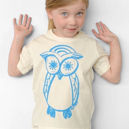 Young girl wearing a cream-colored Uni-T organic cotton t-shirt featuring a blue hand-illustrated owl graphic.