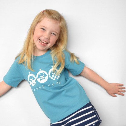 A happy young girl wearing a Uni-T blue organic cotton t-shirt with a white Laugh More graphic print.