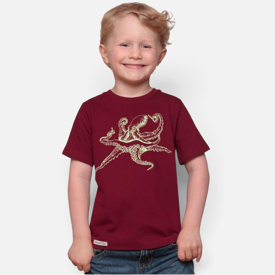A smiling child wearing a Uni-T maroon organic cotton t-shirt featuring a detailed hand-illustrated octopus graphic.