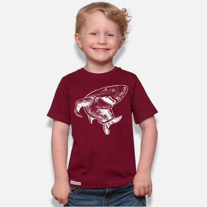 Uni-T kids organic cotton maroon t-shirt featuring a white hand-illustrated shark graphic worn by a smiling boy