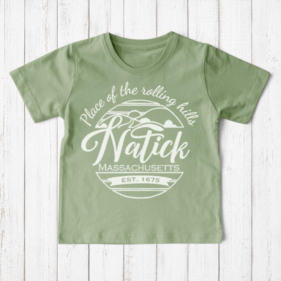 Uni-T sage green organic cotton kids t-shirt with a white Natick Massachusetts graphic print on a wooden background