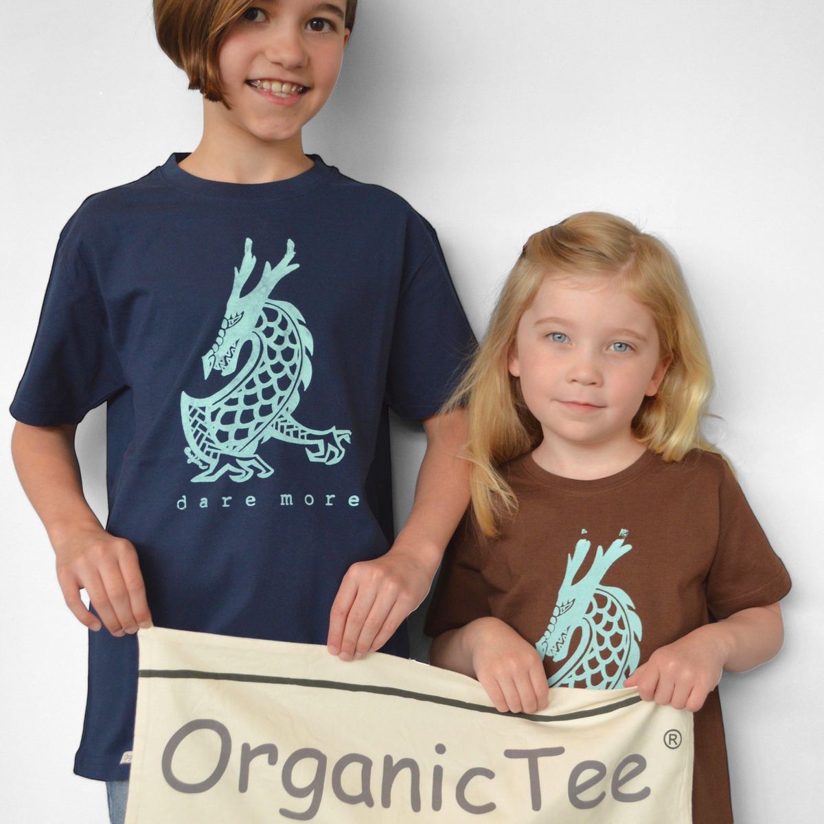 Two children wearing Uni-T organic cotton t-shirts with a teal dragon graphic and Dare More text on navy and brown