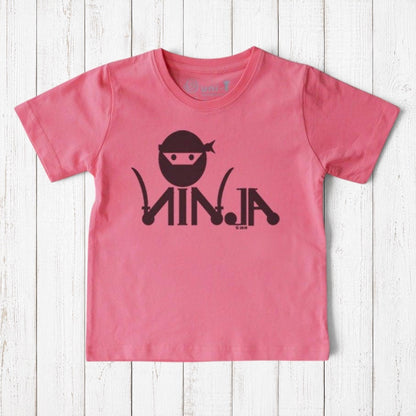 Uni-T pink organic cotton kids t-shirt featuring a black ninja graphic on a white wooden background