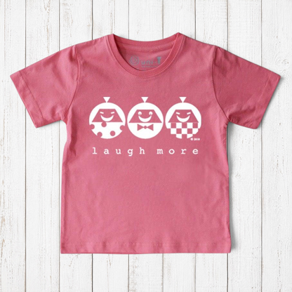 Uni-T organic cotton kids t-shirt in dusty pink with a white Laugh More graphic print on a rustic wood background.