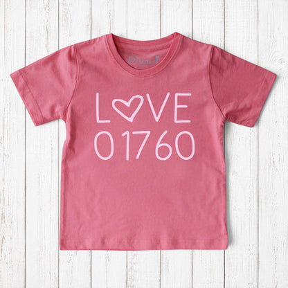 Uni-T kids pink organic cotton t-shirt featuring a white Love 01760 graphic print on a rustic wooden background.
