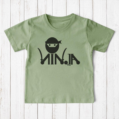 Uni-T sage green organic cotton kids t-shirt with black ninja graphic print on a rustic white wooden background