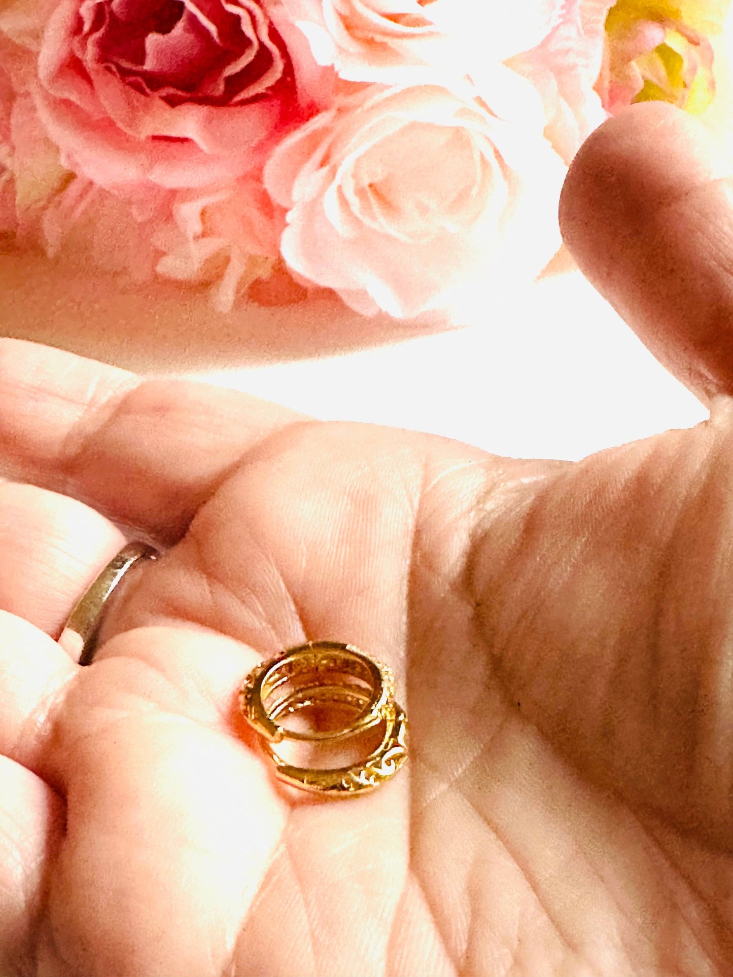 Gold huggie hoop earrings held in hand with floral background, highlighting intricate detailing and elegant craftsmanship.