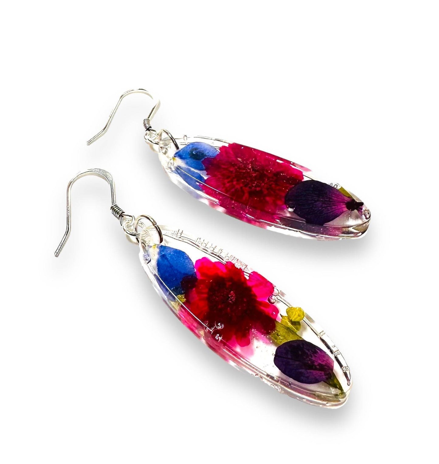 Oval resin earrings with red, blue, and purple real flowers. Silver hooks complete this vibrant floral jewelry piece.