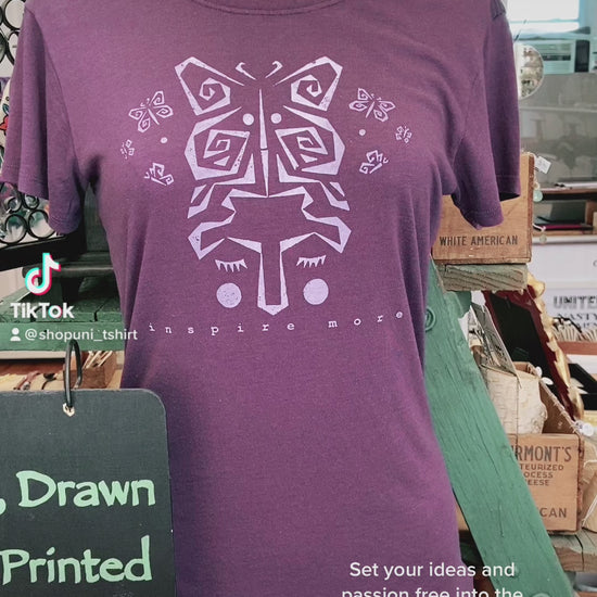 Purple women's bamboo and organic cotton t-shirt on mannequin with lavender butterfly art and 'Inspire More' quote. Displayed in artisan shop setting.