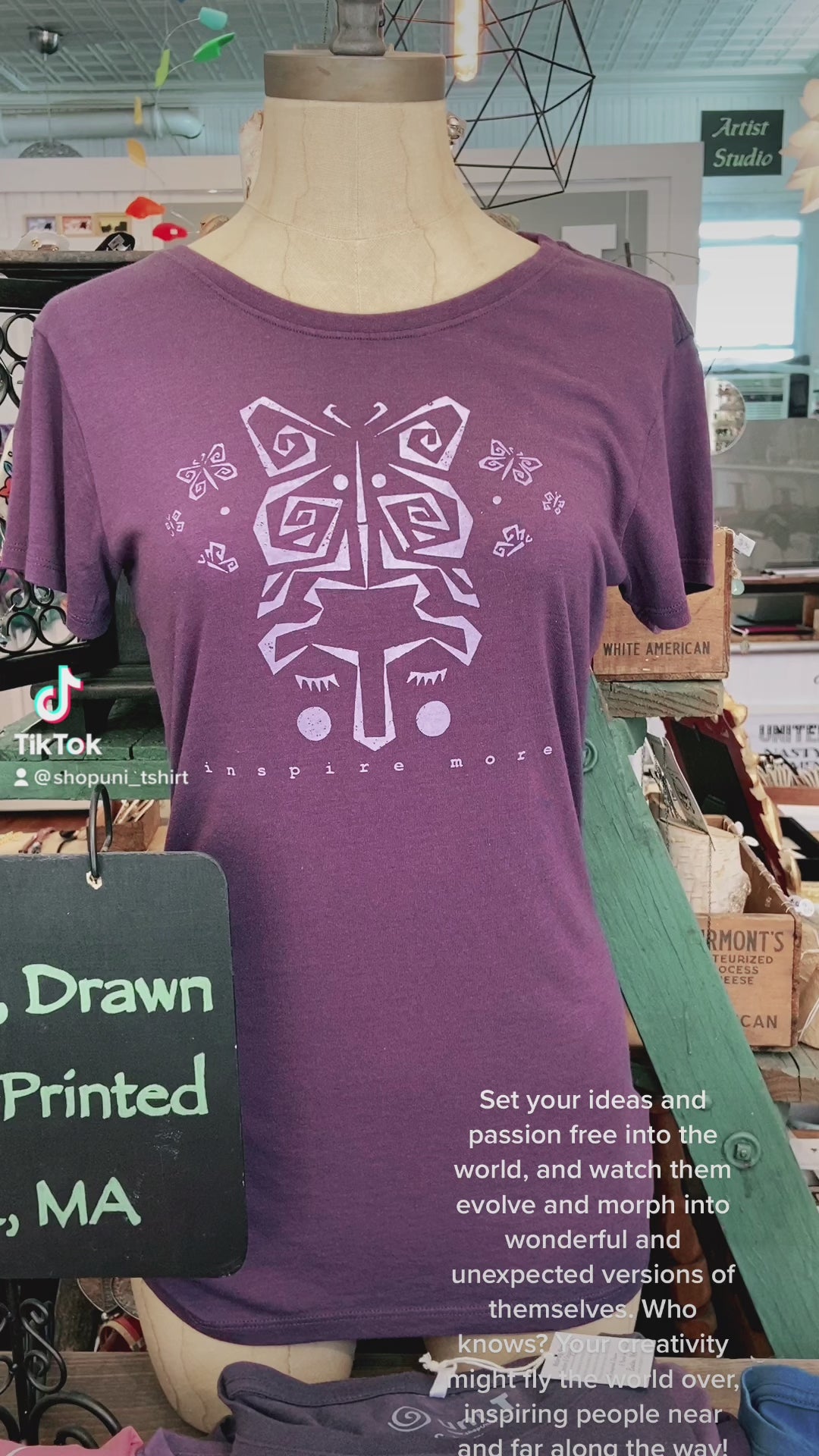 Purple women's bamboo and organic cotton t-shirt on mannequin with lavender butterfly art and 'Inspire More' quote. Displayed in artisan shop setting.