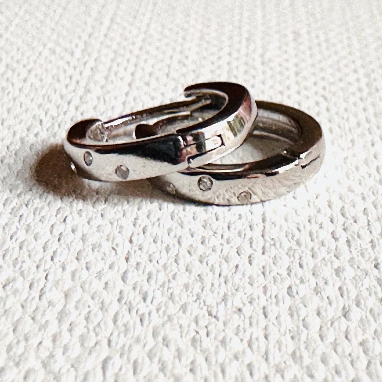 Silver huggie hoop earrings with subtle dot detailing and hinged closures. Sleek and versatile for modern jewelry collections.