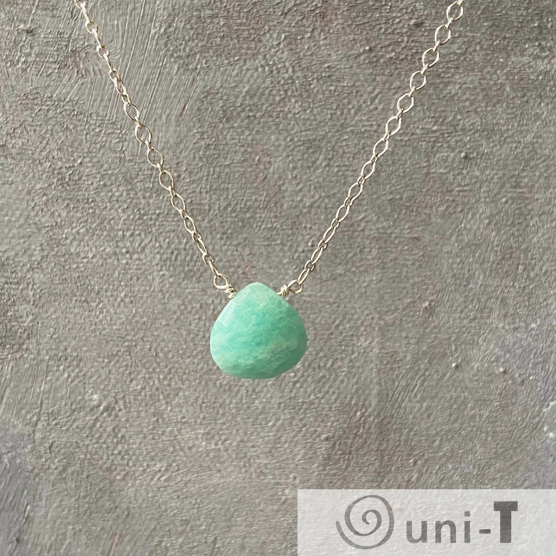 Uni-T Amazonite Gemstone Necklace suspended against a textured gray background, showcasing the minimalist silver chain and vibrant stone.