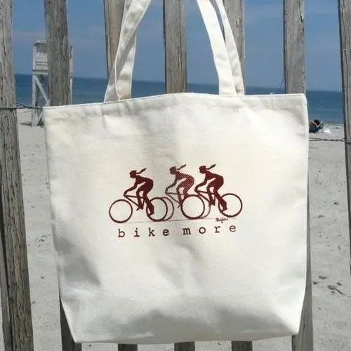 Eco-friendly Cycling Gift Tote Bag with BIKE MORE print shown at the beach. Made from sustainable organic cotton for cyclists on the go.