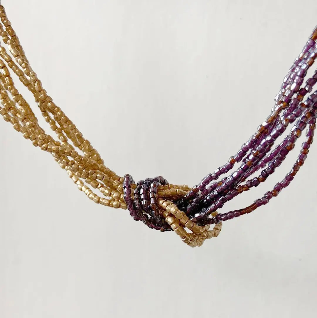 Detailed view of the Beaded Two Tone Knot Necklace's central knot, blending blue metallic and gold beads for a vibrant fashion statement.