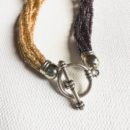Toggle clasp of the Beaded Two Tone Knot Necklace with silver-plated finish, securing multi-strand golden and burgundy beaded necklace.