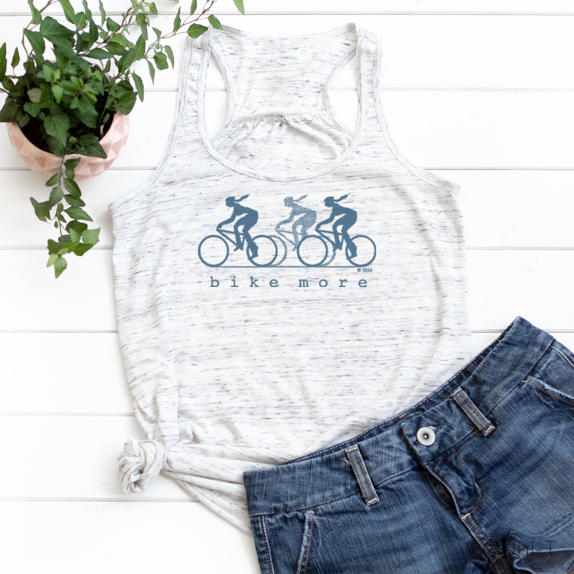 White speckled flowy tank top for women with blue 'bike more' cyclist print, styled with denim shorts for a casual eco-conscious look.